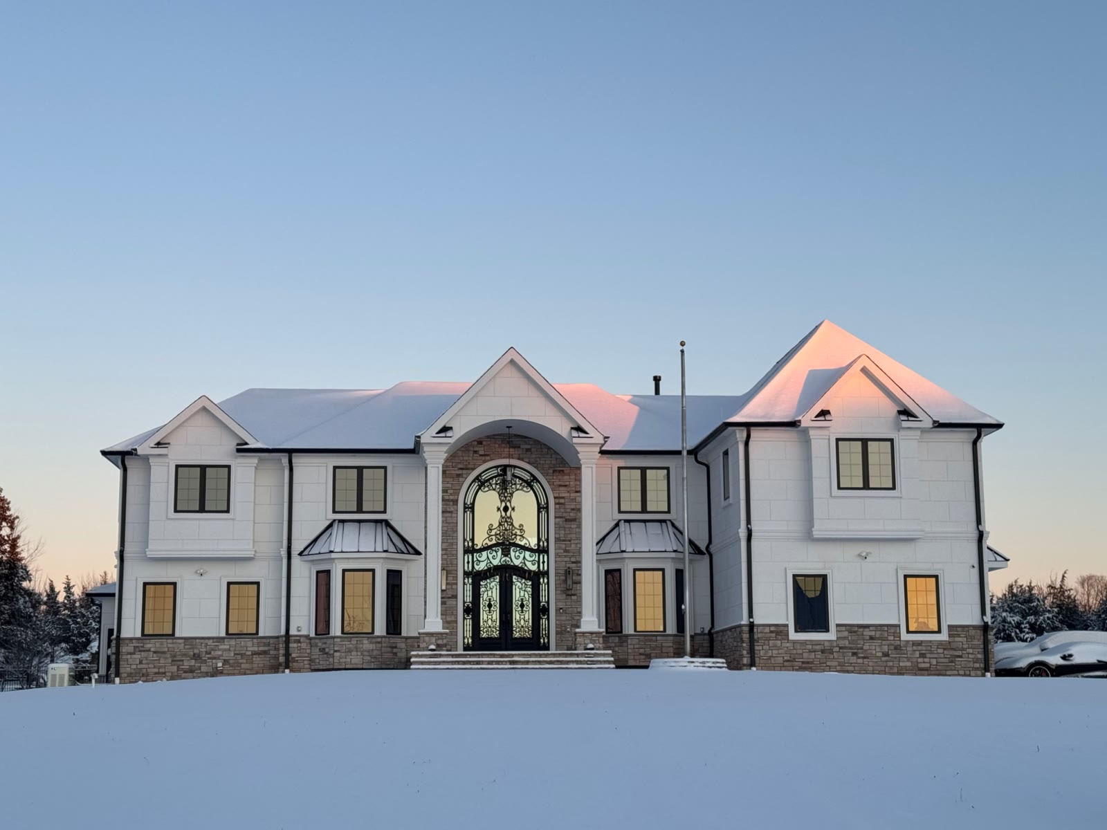The finished residence in fresh snow at sunrise, arched iron entry doors lit from inside