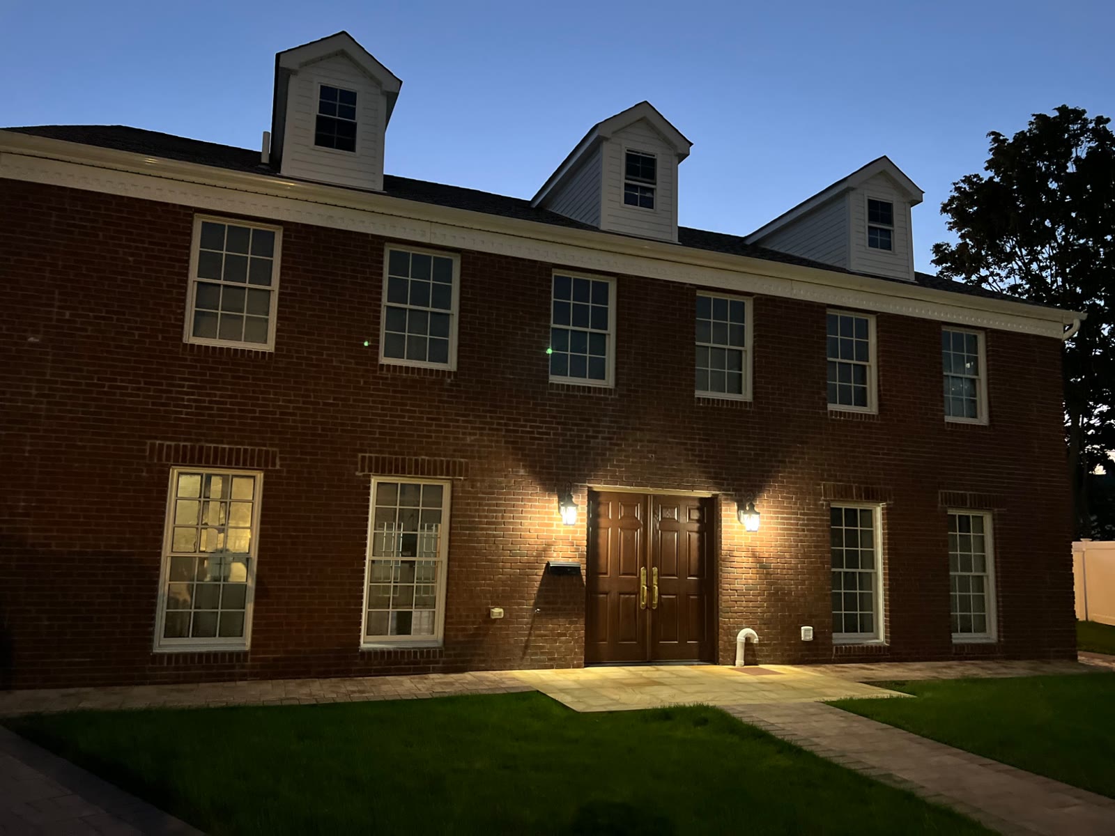 Home renovation: the finished brick home with three dormers, at dusk