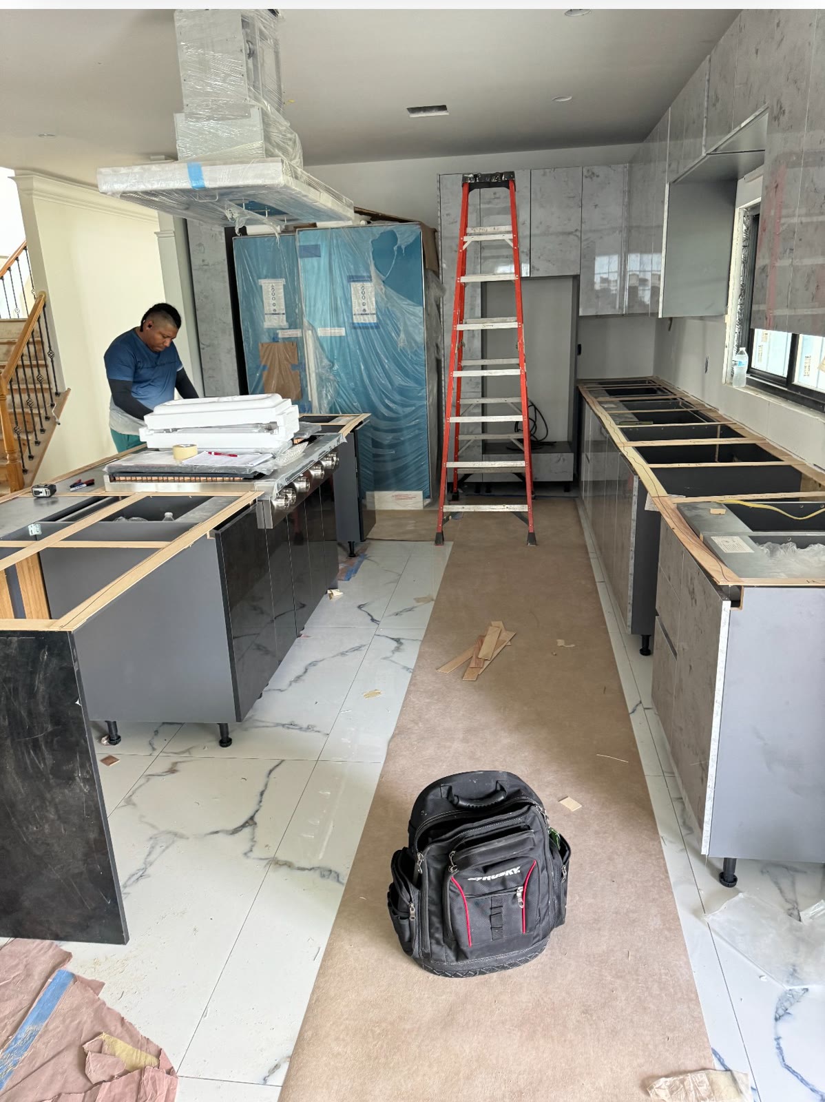 Kitchen being installed, with island, cabinets and marble-look floor tile